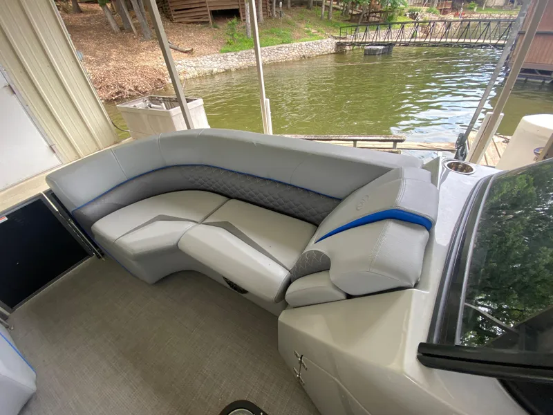 Slide: The Image of 2022 Manitou 25 LX SRW SHP boat interior with gray seating and blue accents by the water. - 26