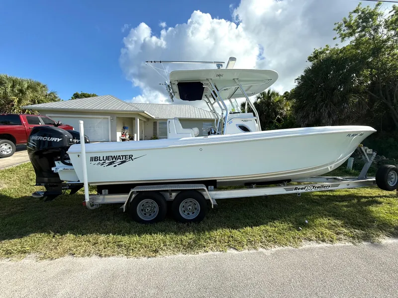 Slide: The Image of 2015 Bluewater 2550 boat on trailer, parked in front of a house, with Mercury engine. - 0