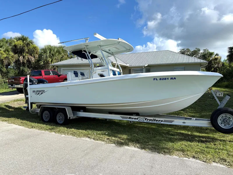 Slide: The Image of 2015 Bluewater 2550 boat on trailer, parked near a house with palm trees. - 1