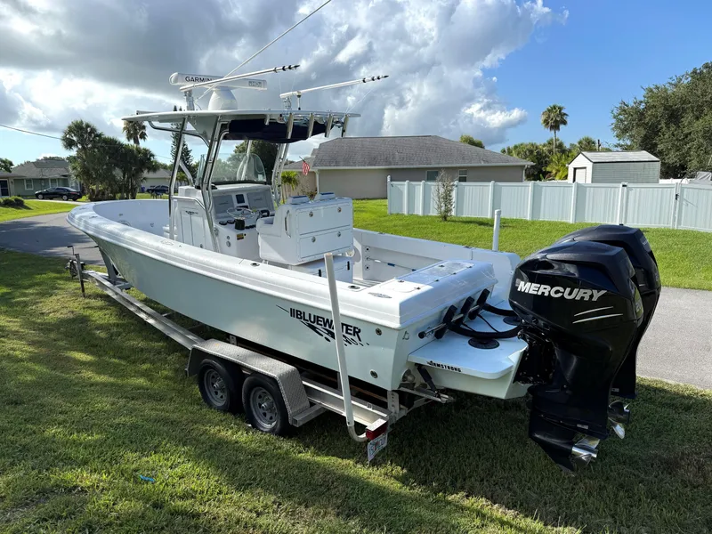 Slide: The Image of 2015 Bluewater 2550 boat with dual Mercury engines on a trailer, parked in a residential area. - 2
