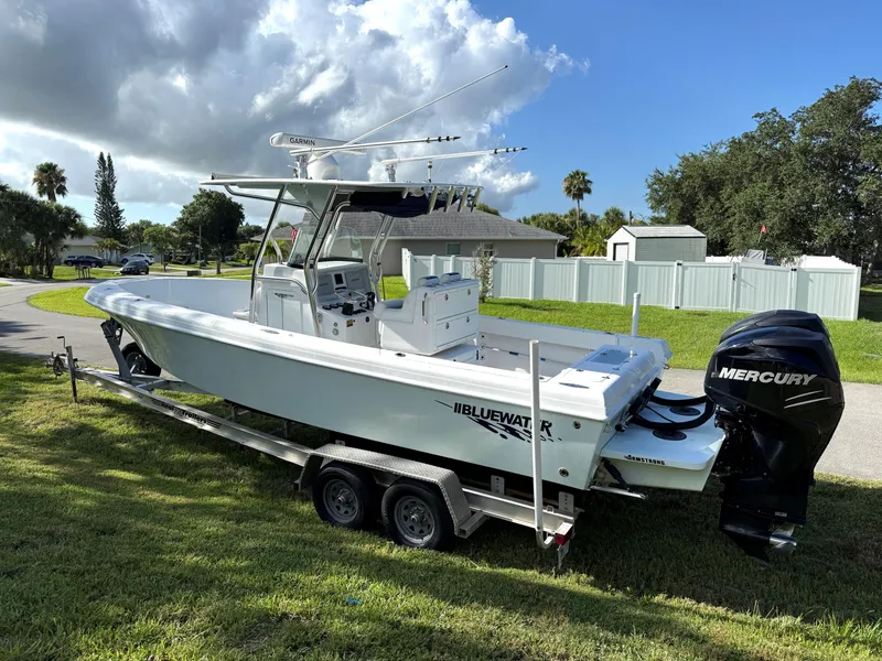 Slide: The Image of 2015 Bluewater 2550 boat on trailer with Mercury engine, parked on grass under cloudy sky. - 4