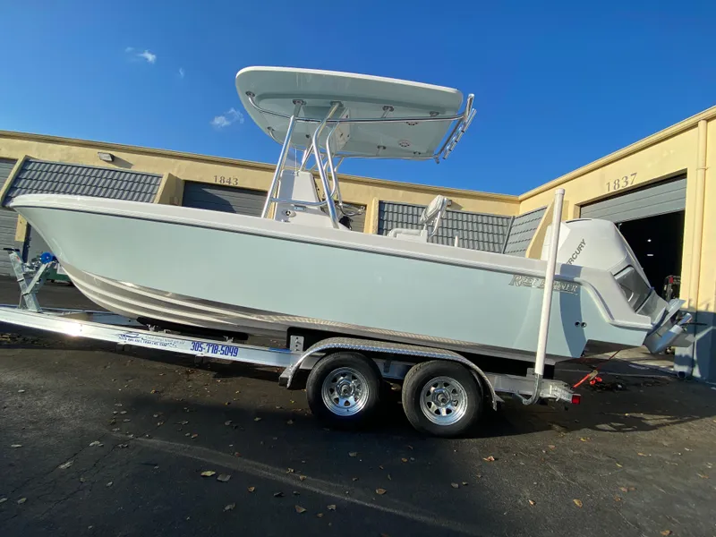 Slide: The Image of 2026 Reef Runner 230 boat on trailer, parked outside industrial building under clear blue sky. - 5