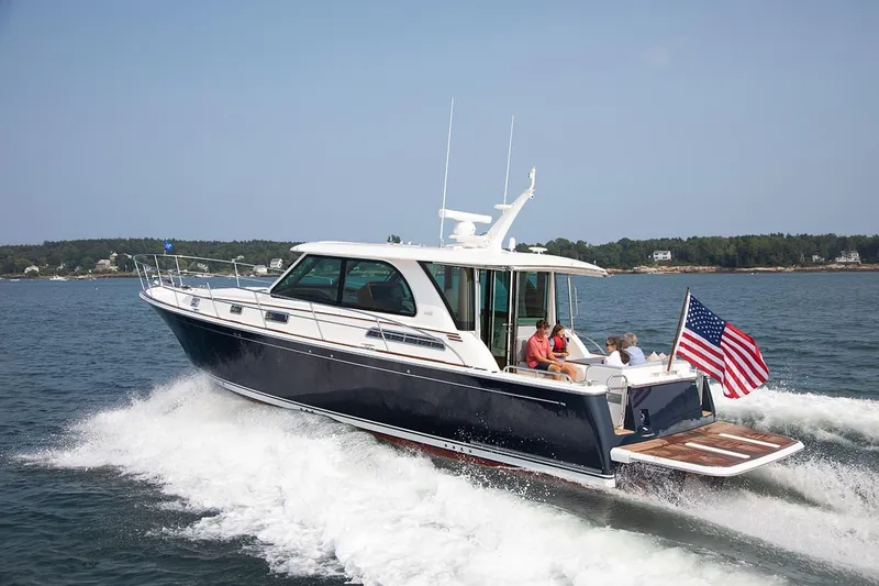 The Image of 2026 Sabre 45 Salon Express yacht cruising with passengers, American flag, scenic coastal background. - 0