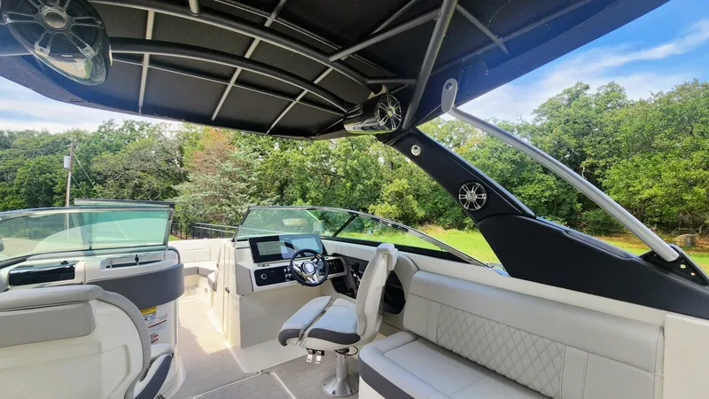 Slide: The Image of 2021 Sea Ray SLX 250 boat interior with modern helm and seating, surrounded by lush greenery. - 15