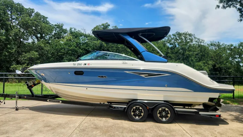 Slide: The Image of 2021 Sea Ray SLX 250 boat on trailer, parked outdoors with trees in background. - 7