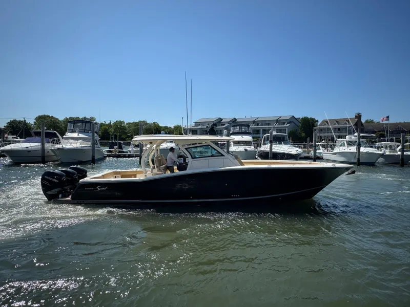 Slide: The Image of 2018 Scout 380 LXF boat cruising in a marina with other boats docked nearby. - 6