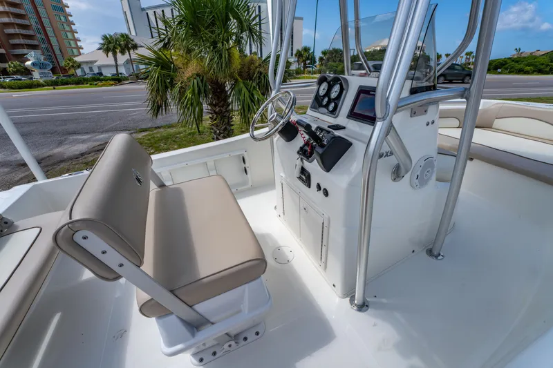 Slide: The Image of 2017 NauticStar 19XS boat interior with steering console and seating, parked near palm trees. - 13