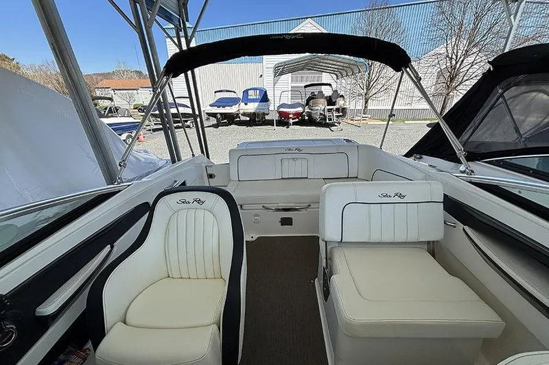Slide: The Image of 2014 Sea Ray 240 Sundeck interior with white seating and canopy in a boatyard. - 32