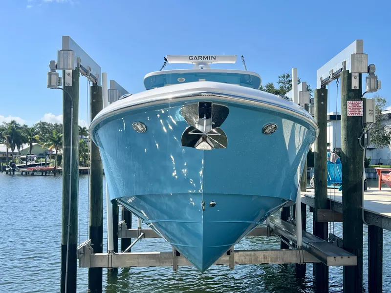 Slide: The Image of 2023 Everglades 365 Center Console boat on lift, blue hull, sunny day, waterfront view. - 36
