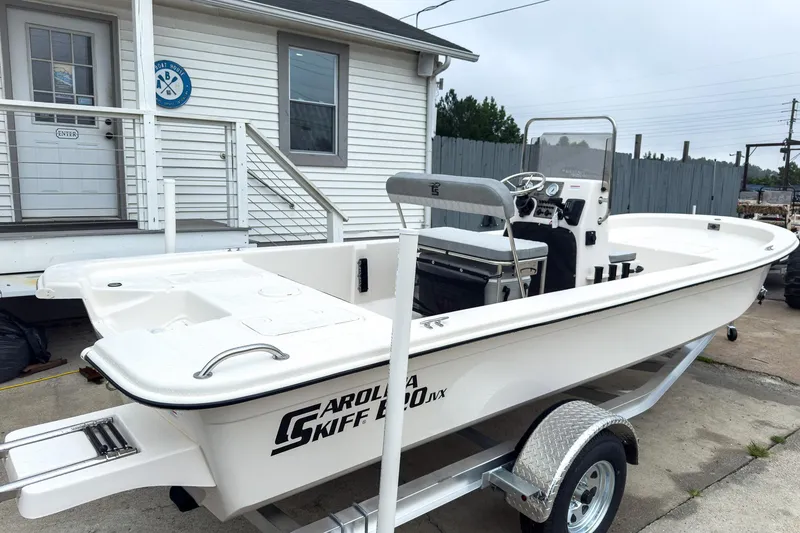 Slide: The Image of 2026 Carolina Skiff E20 JVX CC boat on trailer, parked outside a building. - 2