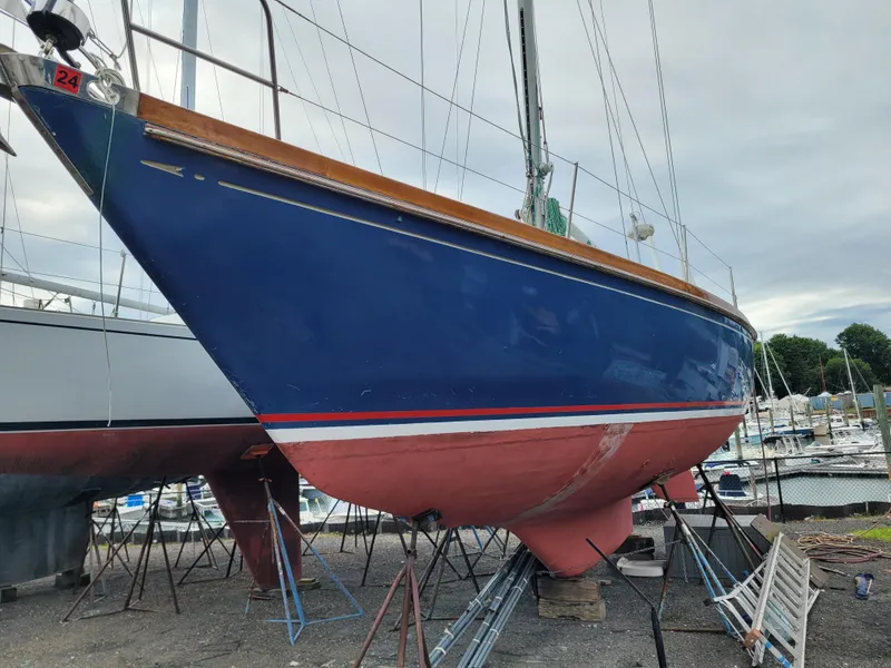 Slide: The Image of 1985 Bristol 38.8 sailboat on dry dock, blue hull, red bottom, overcast sky. - 1