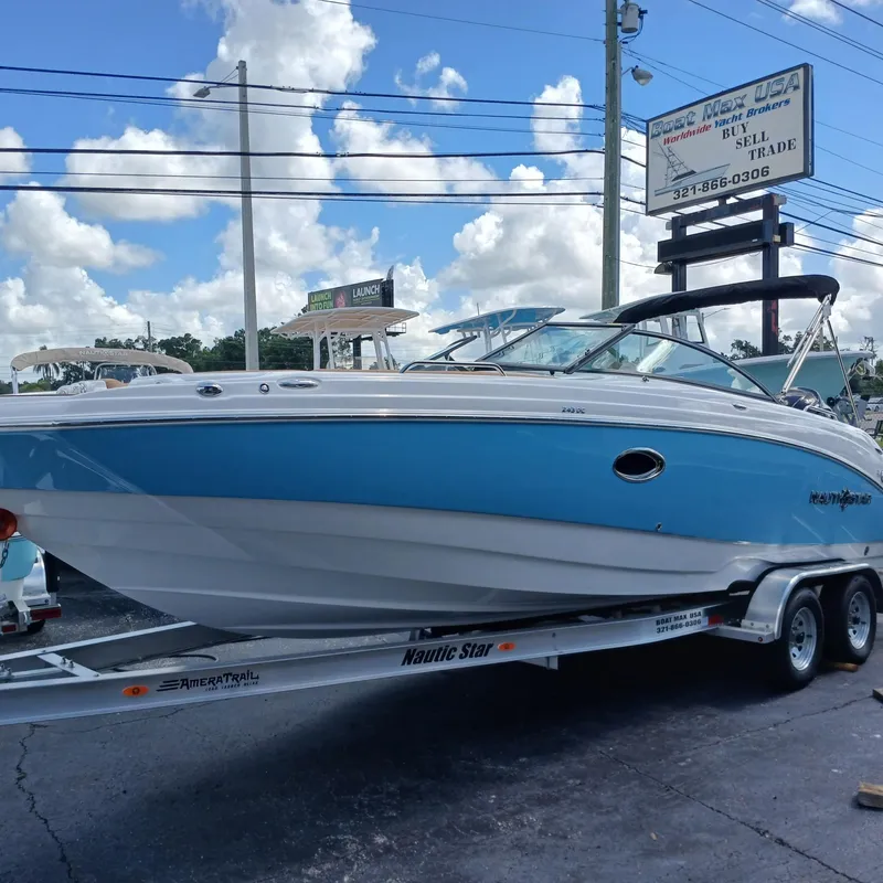 The Image of 2025 NauticStar 243 DC Deck boat on trailer, displayed outdoors under a cloudy sky. - 1