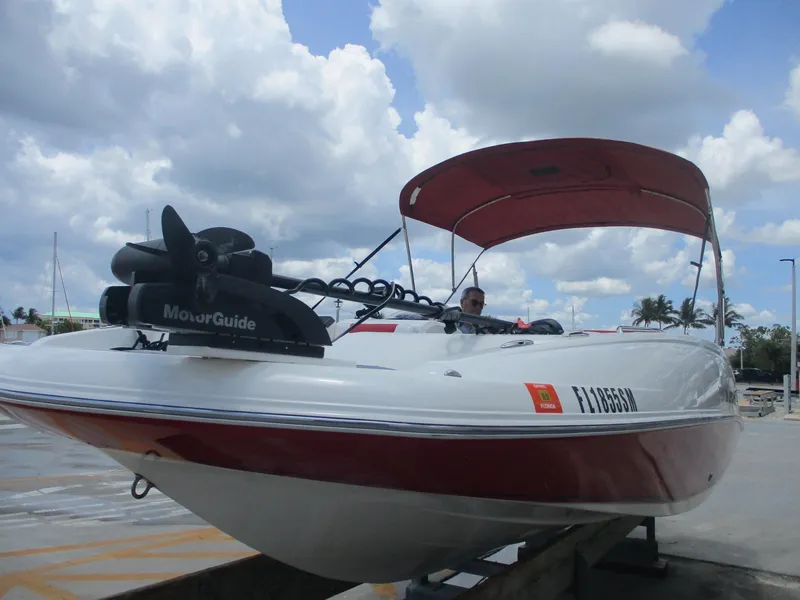 Slide: The Image of 2019 Tahoe 2150 boat with red canopy and MotorGuide motor, docked under cloudy sky. - 1