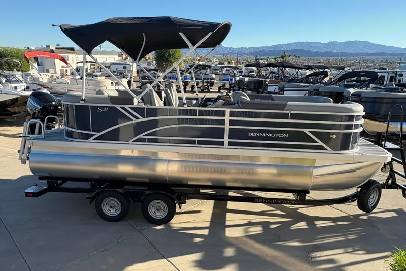 Slide: The Image of 2026 Bennington 21 SSR pontoon boat with canopy on trailer, in a marina setting. - 3