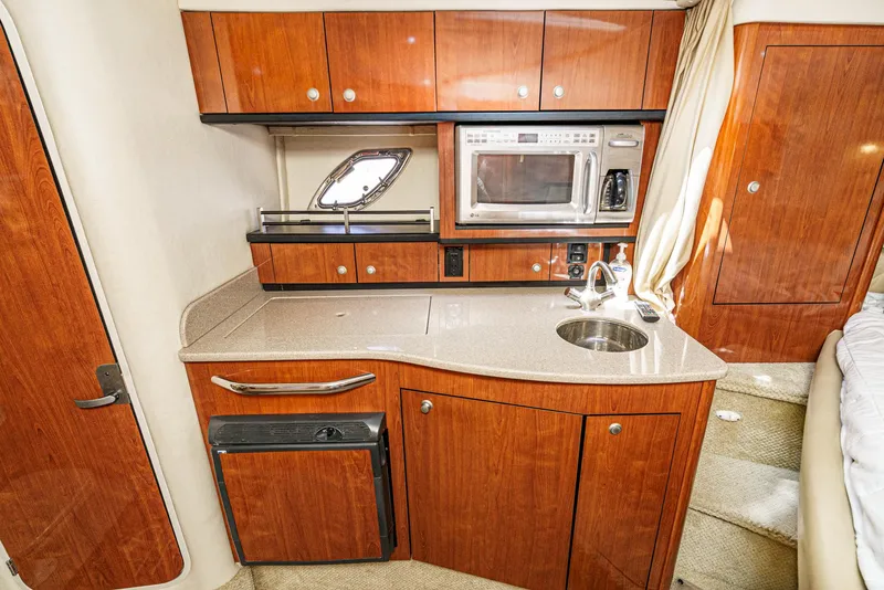 Slide: The Image of 2007 Sea Ray 310 Sundancer galley with wood cabinetry, sink, microwave, and compact fridge. - 26