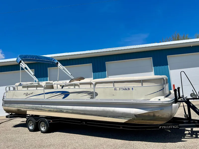 The Image of 2004 Bennington 2875RLX pontoon boat on trailer, parked outside blue building. - 0