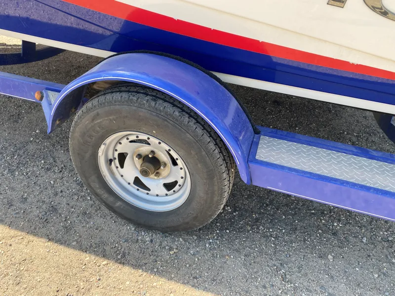 Slide: The Image of 2013 Tahoe Q5i trailer with blue fender and tire on gravel surface. - 13