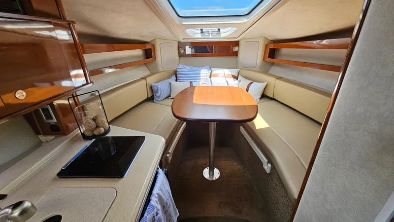 Slide: The Image of 2013 Sea Ray 280 Sundancer cabin interior with seating, table, and skylight. - 19