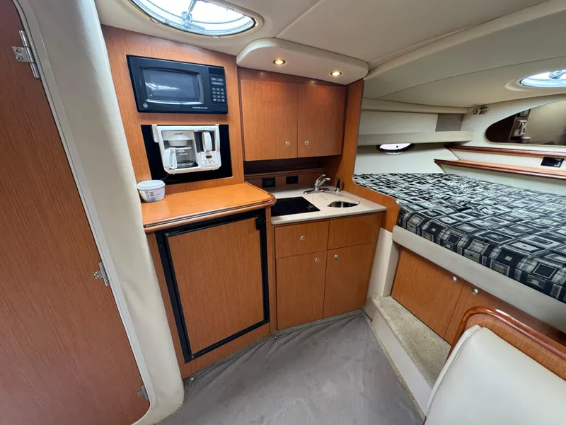 Slide: The Image of 2004 Cruisers Yachts 320 Express interior with kitchenette and bed, featuring wood cabinetry. - 30