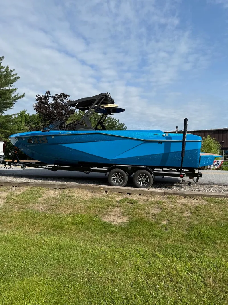 Slide: The Image of Blue 2022 Axis T250 boat on trailer, parked outdoors under a partly cloudy sky. - 6