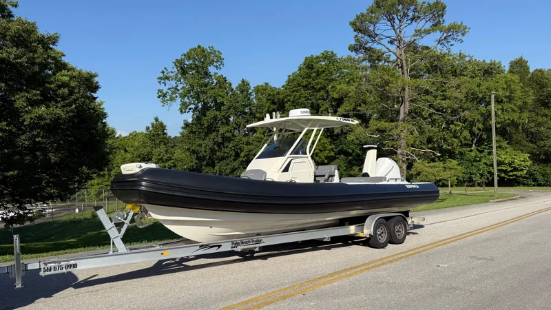 The Image of 2022 Brig Eagle 8 boat on trailer, parked on a road with lush green trees. - 1