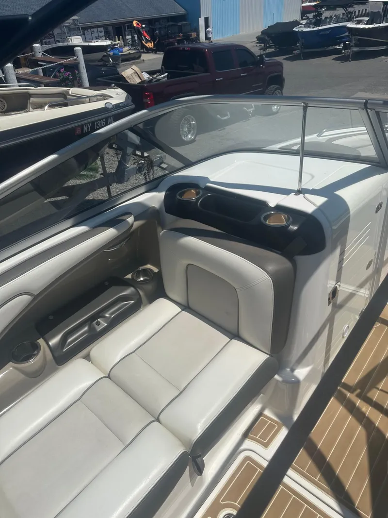 Slide: The Image of 2013 Yamaha Boats 242 Limited S interior with beige seating and dashboard, docked outdoors. - 17