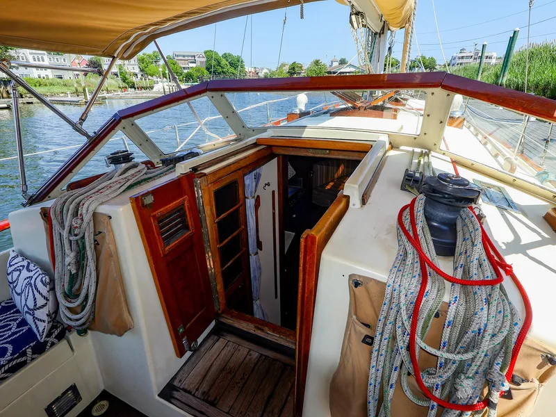 Slide: The Image of 1987 Gozzard 36 sailboat cockpit with ropes and wooden hatch, docked by a scenic waterfront. - 23