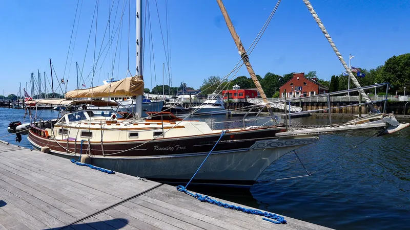 Slide: The Image of 1987 Gozzard 36 sailboat docked at a marina, clear blue sky, calm water. - 33