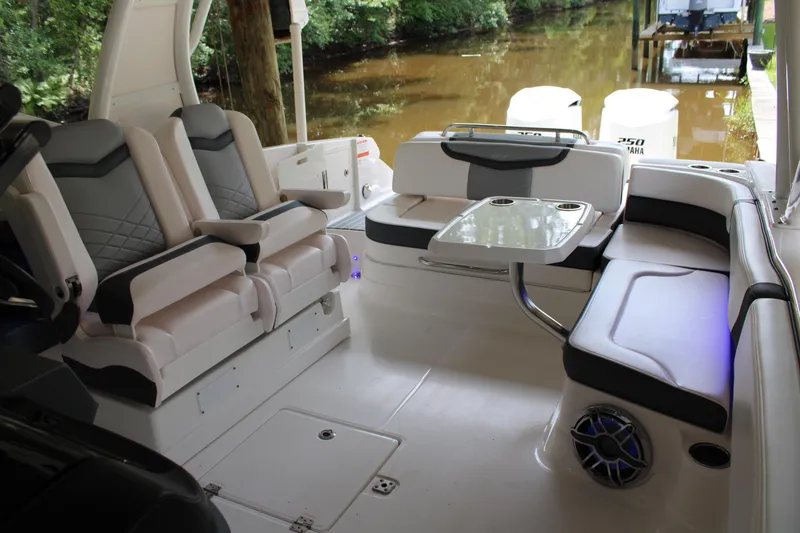Slide: The Image of 2021 Chaparral 280 OSX boat interior with seating and table, docked by a wooded area. - 14