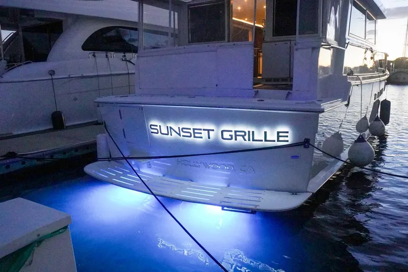 Slide: The Image of 1990 Hatteras 62 Cockpit Motor Yacht docked, illuminated with "Sunset Grille" signage. - 5