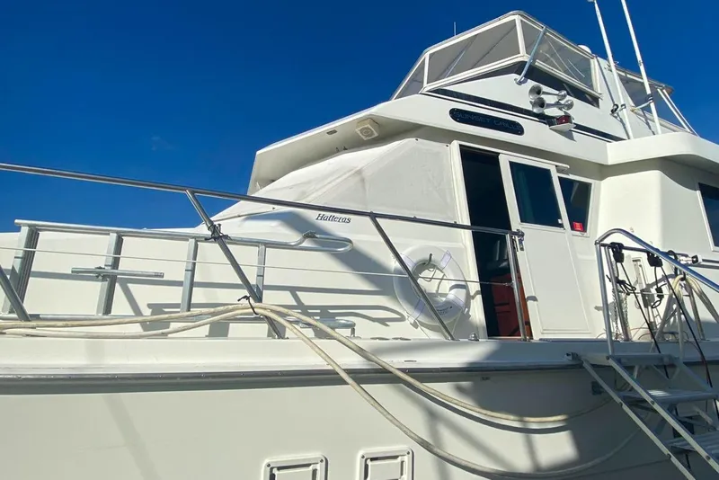 Slide: The Image of 1990 Hatteras 62 Cockpit Motor Yacht with white exterior and railing, under clear blue sky. - 9