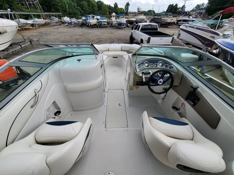 Slide: The Image of 2007 Crownline 220EX boat interior with white seating and dashboard, parked in a marina. - 17