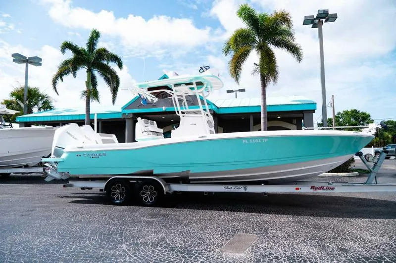 The Image of 2024 Caymas 281 HB boat on trailer, parked near palm trees and a turquoise building. - 0