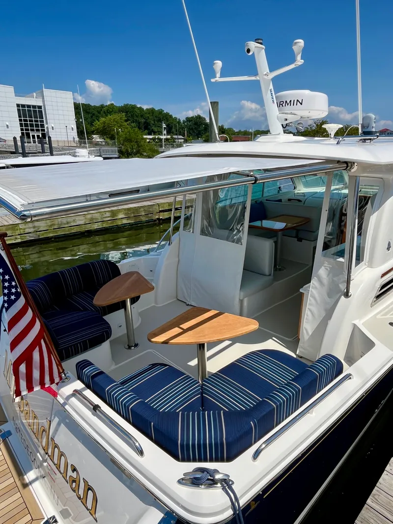 Slide: The Image of 2023 Back Cove 34O yacht with striped seating and American flag, docked under clear skies. - 10