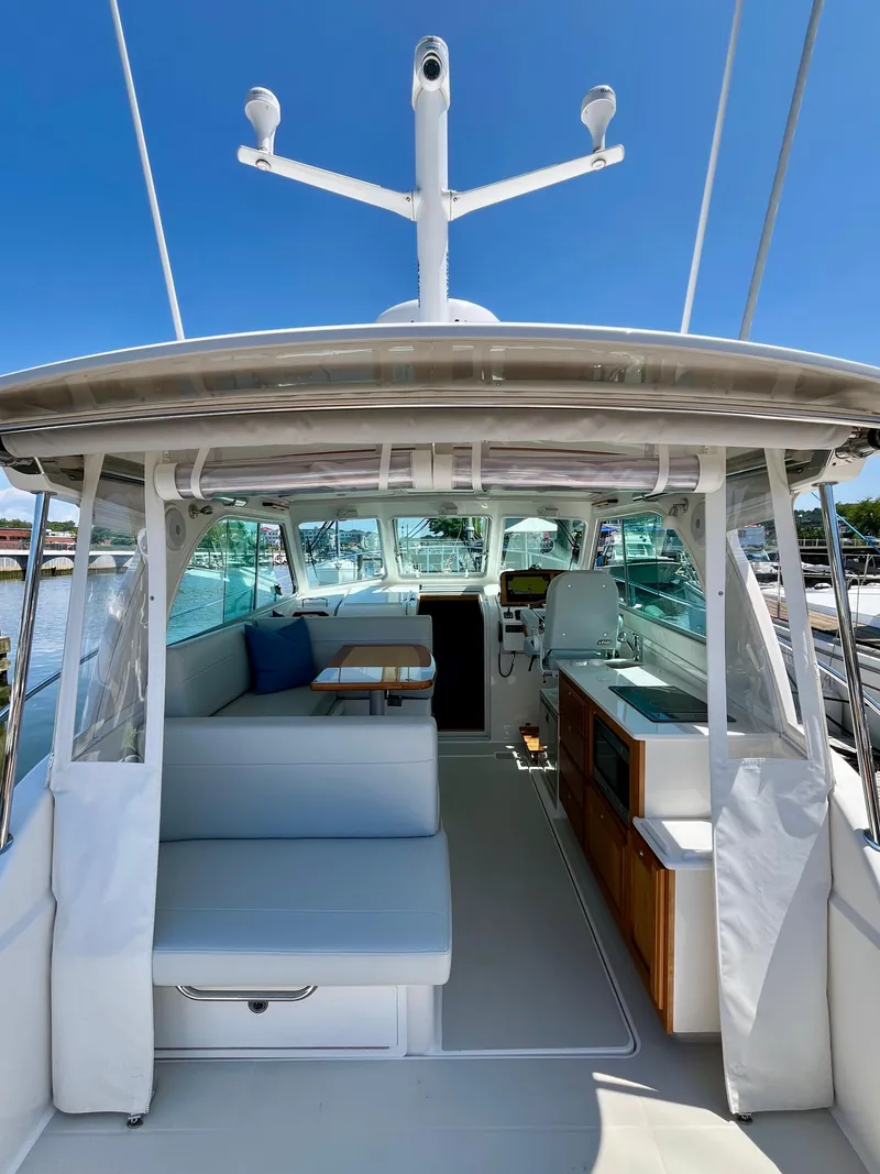Slide: The Image of 2023 Back Cove 34O yacht interior with seating, table, and helm under clear blue sky. - 12