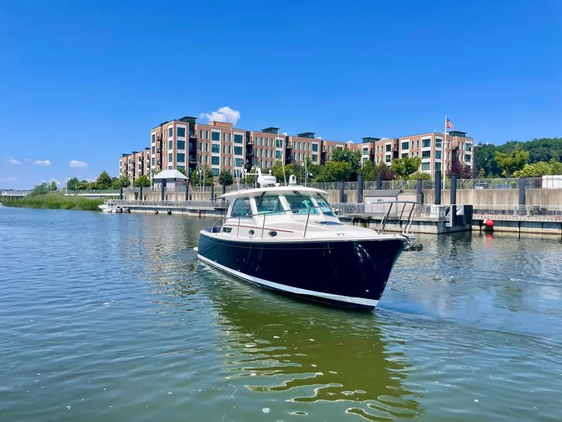 Slide: The Image of 2023 Back Cove 34O boat on a calm river near modern waterfront buildings. - 2