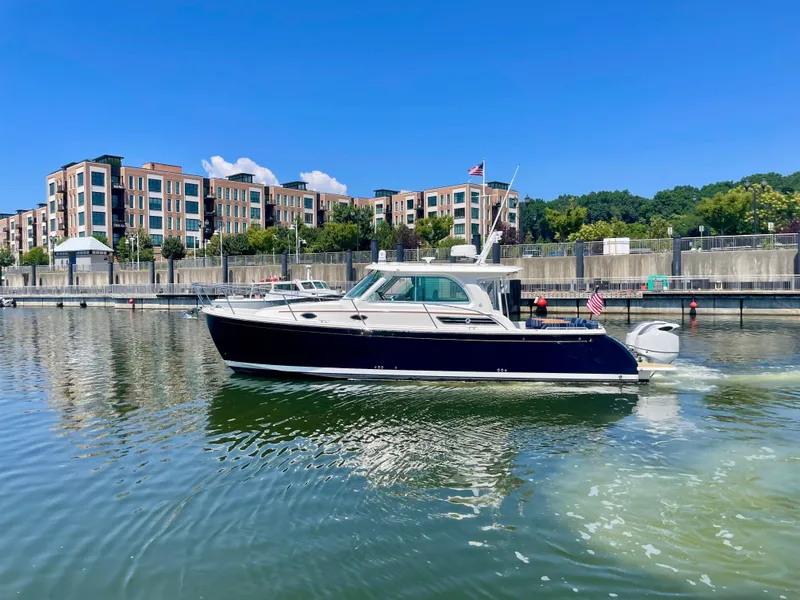 Slide: The Image of 2023 Back Cove 34O boat cruising in a marina with modern buildings in the background. - 3