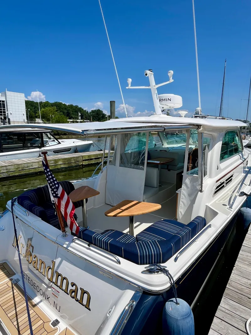 Slide: The Image of 2023 Back Cove 34O yacht docked, featuring a spacious deck with seating and an American flag. - 8