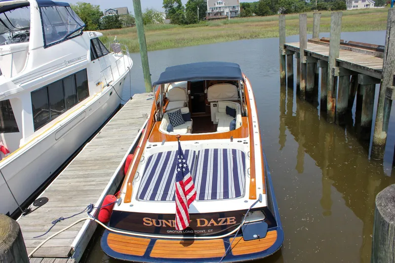 Slide: The Image of 2008 Hinckley Talaria 38R Convertible docked, featuring striped seating and American flag. - 2