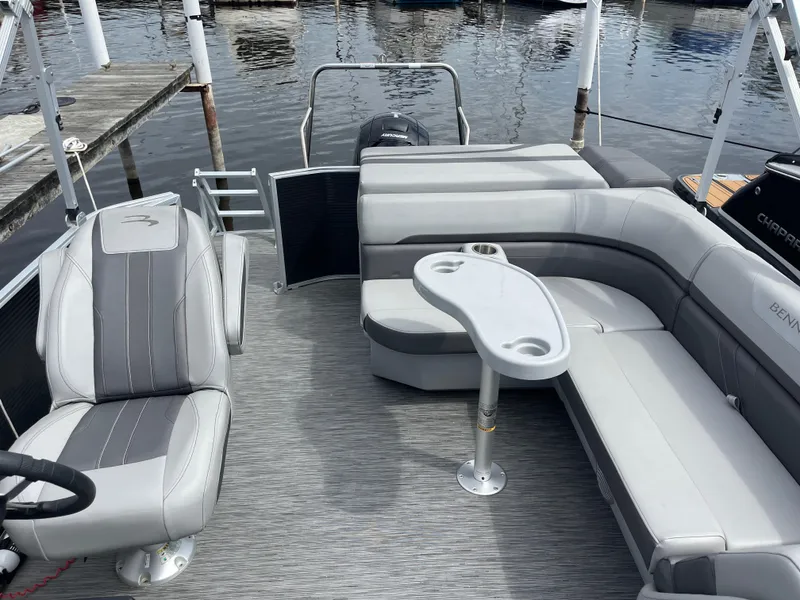 Slide: The Image of 2022 Bennington 21 SX pontoon boat interior with gray seating and table, docked by the water. - 17