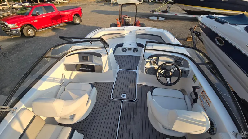Slide: The Image of 2022 Hurricane SunDeck 191 OB boat interior with steering wheel and seating, parked near red truck. - 16