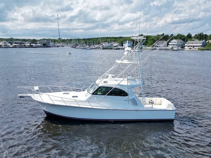 Slide: The Image of 2022 Henriques 42 Express Hardtop boat on calm water, with coastal houses in the background. - 2