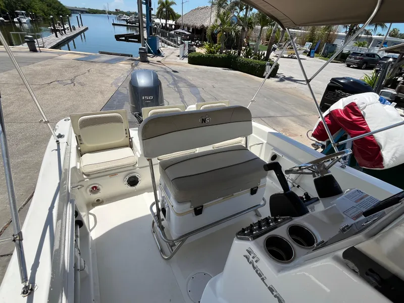 Slide: The Image of 2016 NauticStar 211 Angler boat interior at marina, featuring seating and steering console. - 7