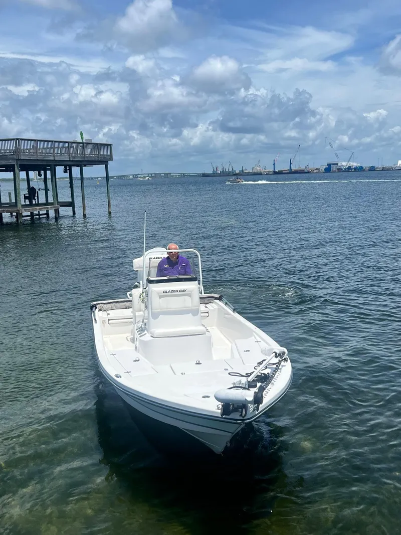 Slide: The Image of 2021 Blazer Bay 2200 boat on water near dock under cloudy sky. - 2