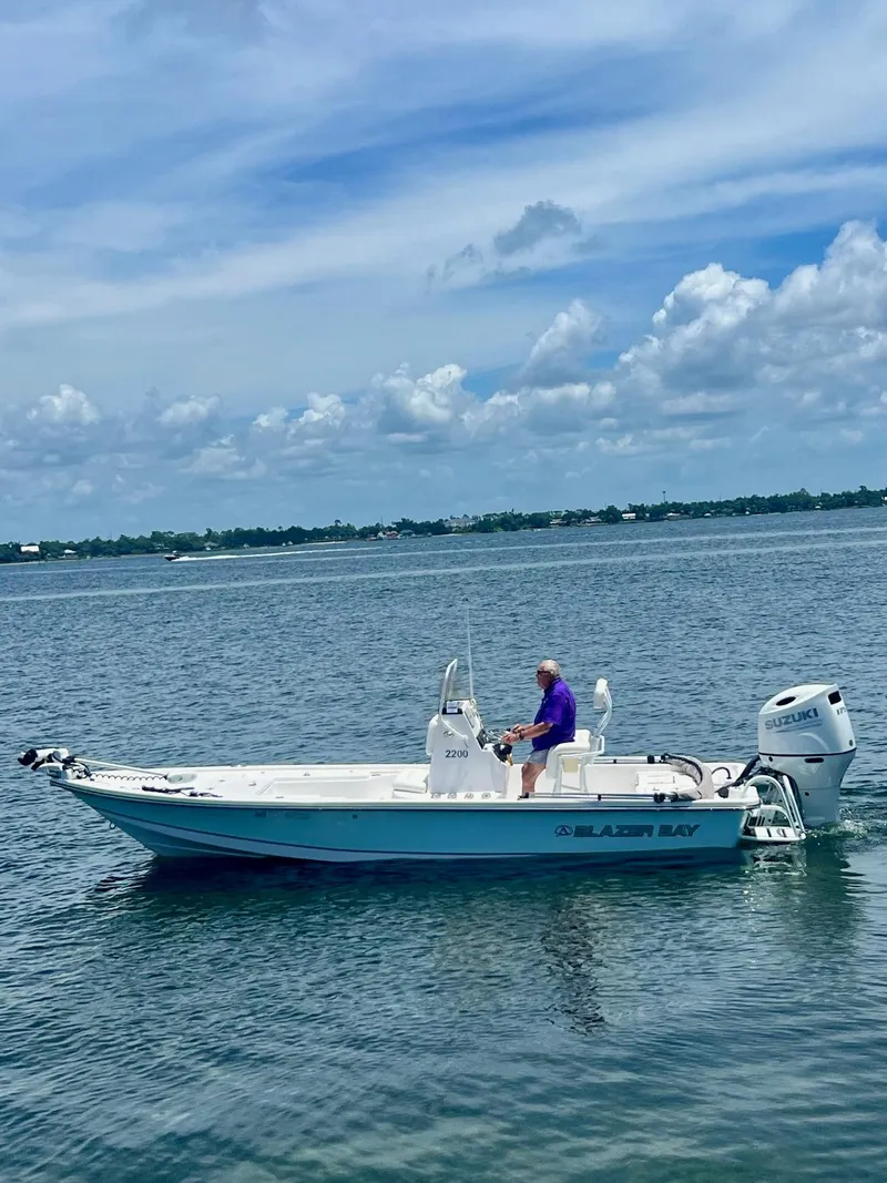 Slide: The Image of 2021 Blazer Bay 2200 boat on calm water with person seated, under a partly cloudy sky. - 4