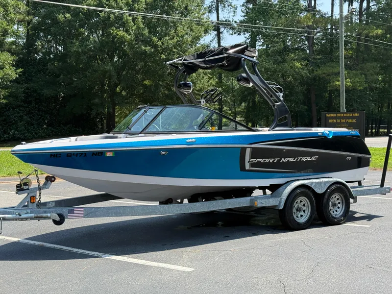 Slide: The Image of 2014 Nautique Sport 200 boat on trailer, parked outdoors, surrounded by trees. - 23