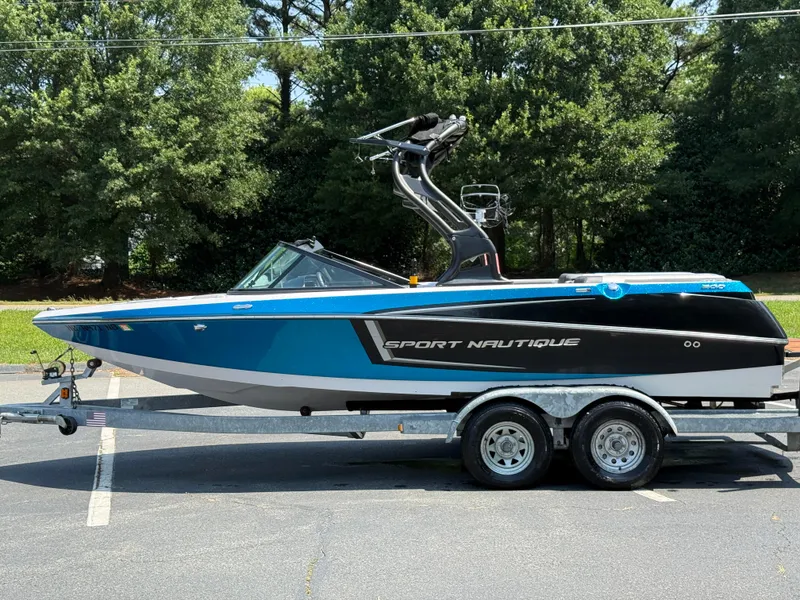Slide: The Image of 2014 Nautique Sport 200 boat on trailer, parked outdoors with trees in background. - 24