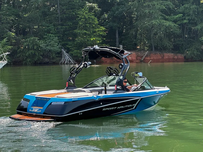 Slide: The Image of 2014 Nautique Sport 200 boat cruising on a serene lake with lush forest backdrop. - 3