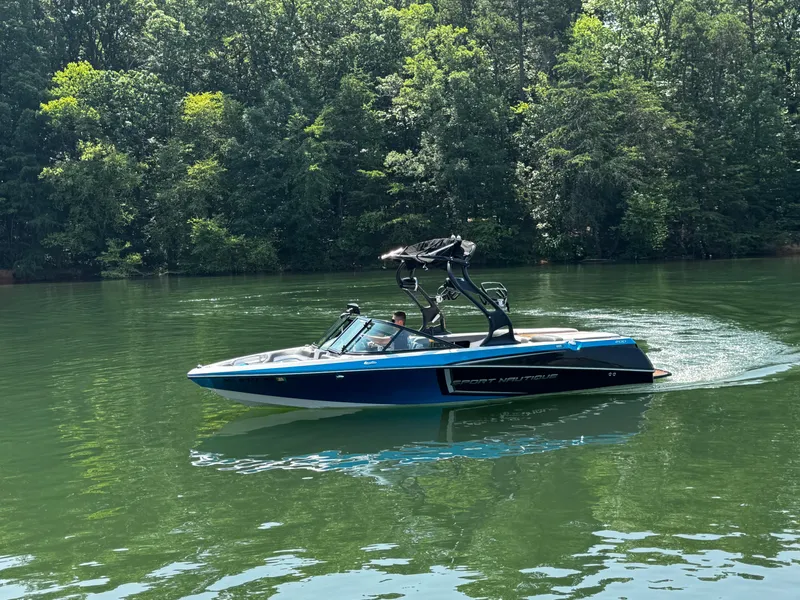 Slide: The Image of 2014 Nautique Sport 200 boat cruising on a serene lake surrounded by lush trees. - 6