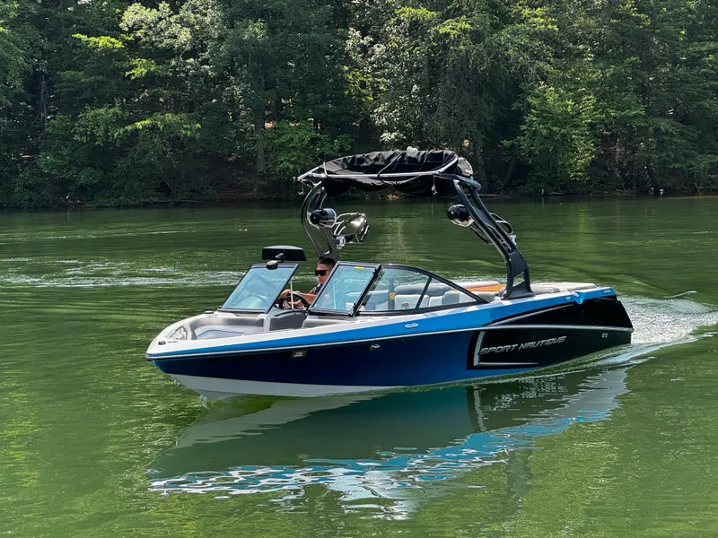 Slide: The Image of 2014 Nautique Sport 200 boat cruising on a serene lake surrounded by lush greenery. - 7